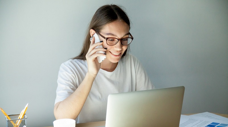 Millennial woman in glasses talking on mobile and using laptop